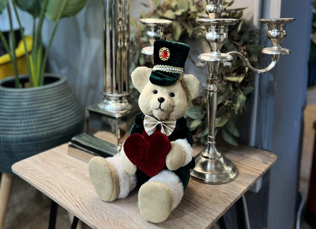 Dressed bear with heart presented next to silver candles and on a wooden top