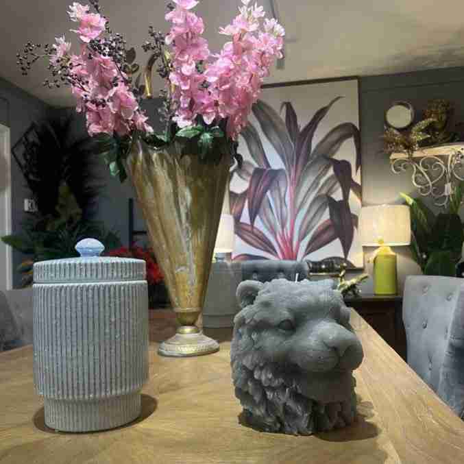 Large tiger head candle on a kitchen table next to luxurious flowers.